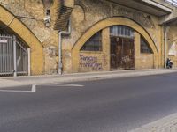 a street with two buildings and graffiti on the walls with old doors and windows that are leaning against each other