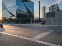 a car is parked at an intersection next to a tall glass building with a sky background