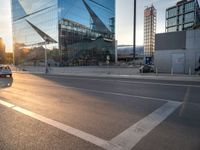 a car is parked at an intersection next to a tall glass building with a sky background