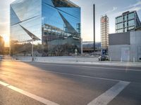 a car is parked at an intersection next to a tall glass building with a sky background