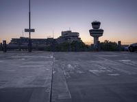 two cars parked in a parking lot beside a control tower and other buildings at dusk