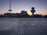 two cars parked in a parking lot beside a control tower and other buildings at dusk