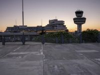 two cars parked in a parking lot beside a control tower and other buildings at dusk