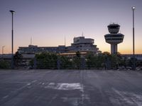 two cars parked in a parking lot beside a control tower and other buildings at dusk