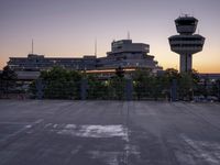 two cars parked in a parking lot beside a control tower and other buildings at dusk