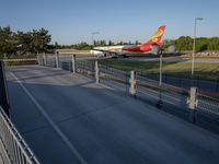 a long red and orange airplane on a tarmac next to a fence and trees