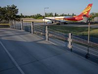 a long red and orange airplane on a tarmac next to a fence and trees