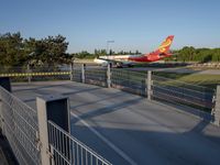 a long red and orange airplane on a tarmac next to a fence and trees