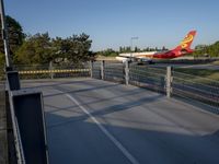 a long red and orange airplane on a tarmac next to a fence and trees