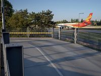 a long red and orange airplane on a tarmac next to a fence and trees