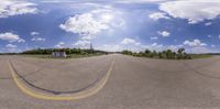 a fish eye view shows the intersection of the road and house in it, with clouds in the sky and a light blue sky above