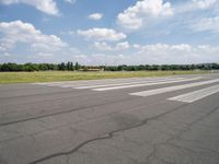 a deserted airport runway with some cars and grass around it at an airfield in summer