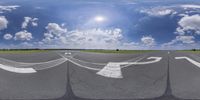 four white painted arrows on an air strip above some grass and sky and clouds with sunlight shining in the background