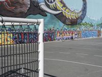 an elephant mural on the side of a tennis court in a parking lot next to a metal fence