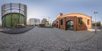 a panorama of a brick building in a large square, surrounded by several smaller buildings, in the middle of the road