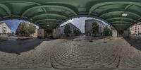 a panoramic view looking through an arch over a square with benches and stairs