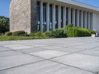 a concrete floor in front of a large building with lots of windows and some bushes