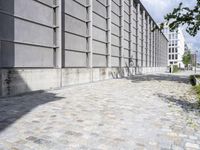 the sidewalk is lined with brick tiles next to the tall building and has windows on it