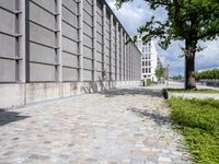 the sidewalk is lined with brick tiles next to the tall building and has windows on it