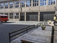 the red bus is next to the empty building, and an empty patio with flowers in the vase