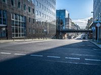 the empty road is surrounded by tall buildings in the area, which has a bridge in the middle of it