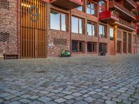 the brick walkway next to the red building is lined with windows and potted plants