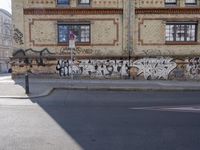 a graffiti covered wall near a road next to a building with windows and a fire hydrant