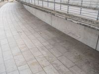 a young man rides his skateboard across the sidewalk next to a railing that is covered by cement and bricks