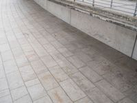 a young man rides his skateboard across the sidewalk next to a railing that is covered by cement and bricks