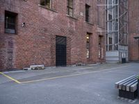 a bench sits in front of a brick building next to a parking space with a fire escaper