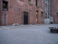 a bench sits in front of a brick building next to a parking space with a fire escaper