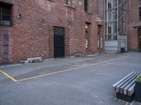 a bench sits in front of a brick building next to a parking space with a fire escaper