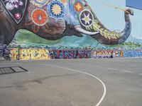 a mural on the side of a large building next to an elephant statue on a basketball court