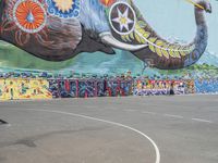 a mural on the side of a large building next to an elephant statue on a basketball court