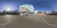 a view of an artistic wall on a parking lot with a skate board in the middle