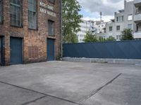 a basketball court with black fence around it in front of brick building and tall buildings