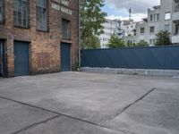 a basketball court with black fence around it in front of brick building and tall buildings