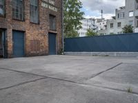 a basketball court with black fence around it in front of brick building and tall buildings