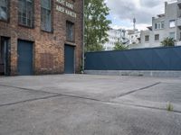 a basketball court with black fence around it in front of brick building and tall buildings