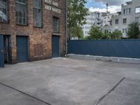 a basketball court with black fence around it in front of brick building and tall buildings