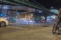 a woman with a bike stands on a city street during the night with an urban bridge above