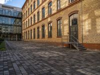 a sidewalk with chairs next to the brick building on the side, some have stairs and some buildings in the background