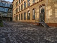 a sidewalk with chairs next to the brick building on the side, some have stairs and some buildings in the background