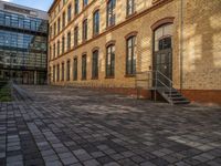 a sidewalk with chairs next to the brick building on the side, some have stairs and some buildings in the background