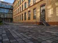 a sidewalk with chairs next to the brick building on the side, some have stairs and some buildings in the background