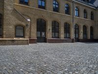 the sidewalk is paved with stones and has a bench in front of it, with no people inside