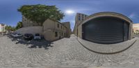 two buildings and cars in a street near the sun and blue sky in a circular panorama