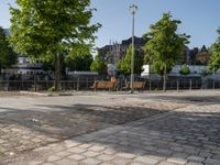 an empty park on the corner of a street next to a fence and benches in a city