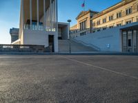 empty street lined with cement buildings next to a tall building with a staircase up to it