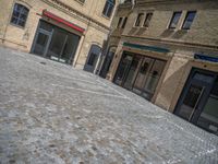 the sidewalk is paved with stones and has a bench in front of it, with no people inside